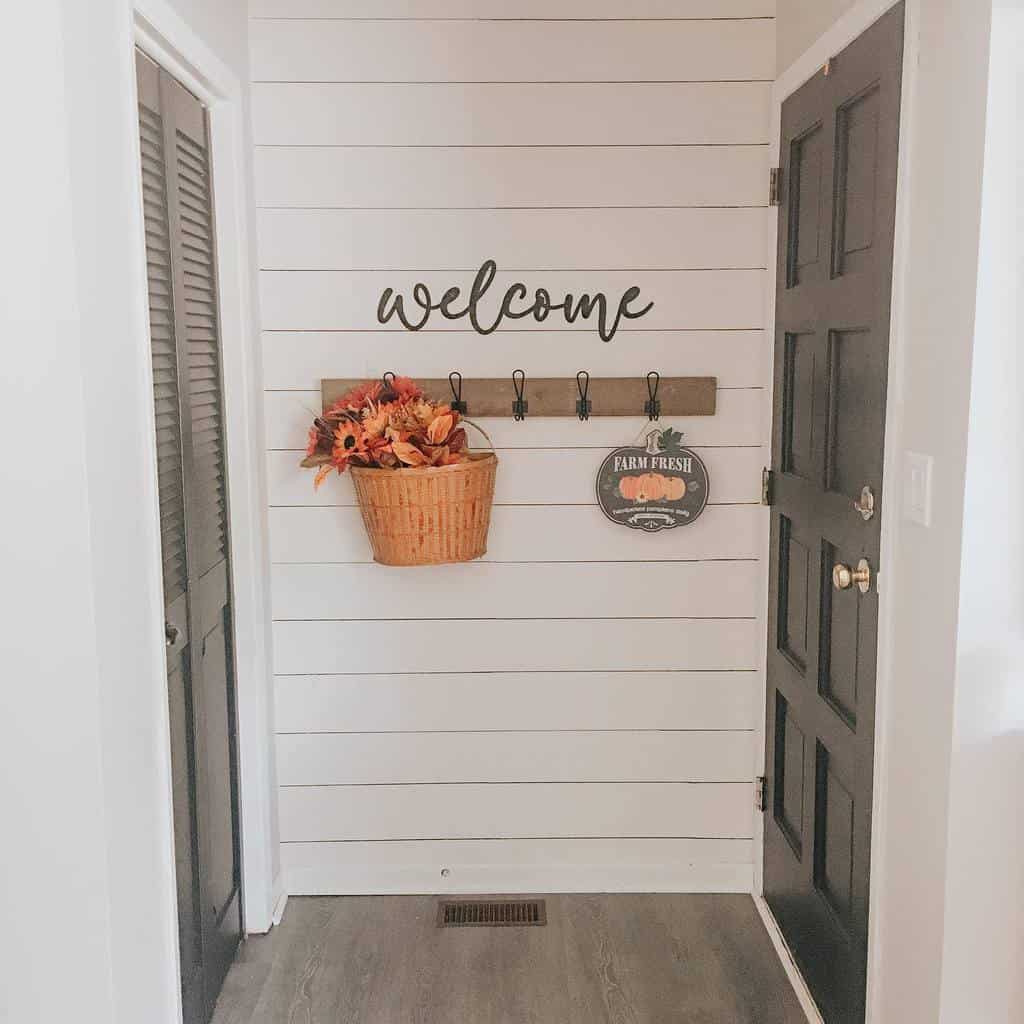 Farmhouse-style entryway with shiplap walls, a wooden coat rack, a 'welcome' sign, and a fall-themed basket for a warm, inviting touch