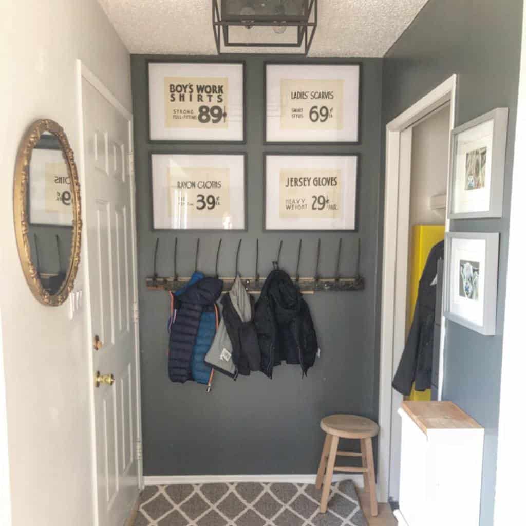 Functional entryway with dark walls, a wooden coat rack, vintage-style framed prints, a patterned rug, and a small wooden stool