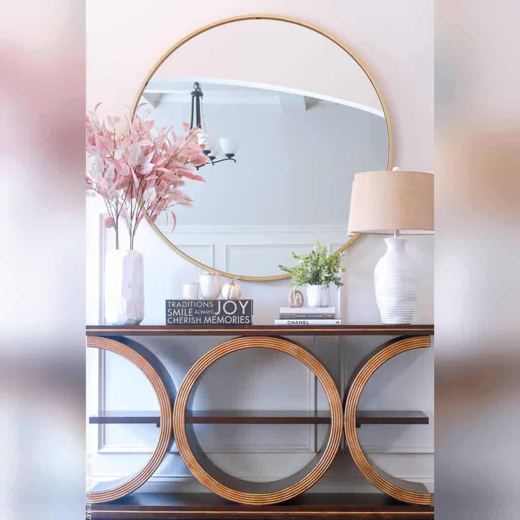 Elegant entryway with a statement console table, large round mirror, soft pink florals, and decorative accents for a sophisticated look