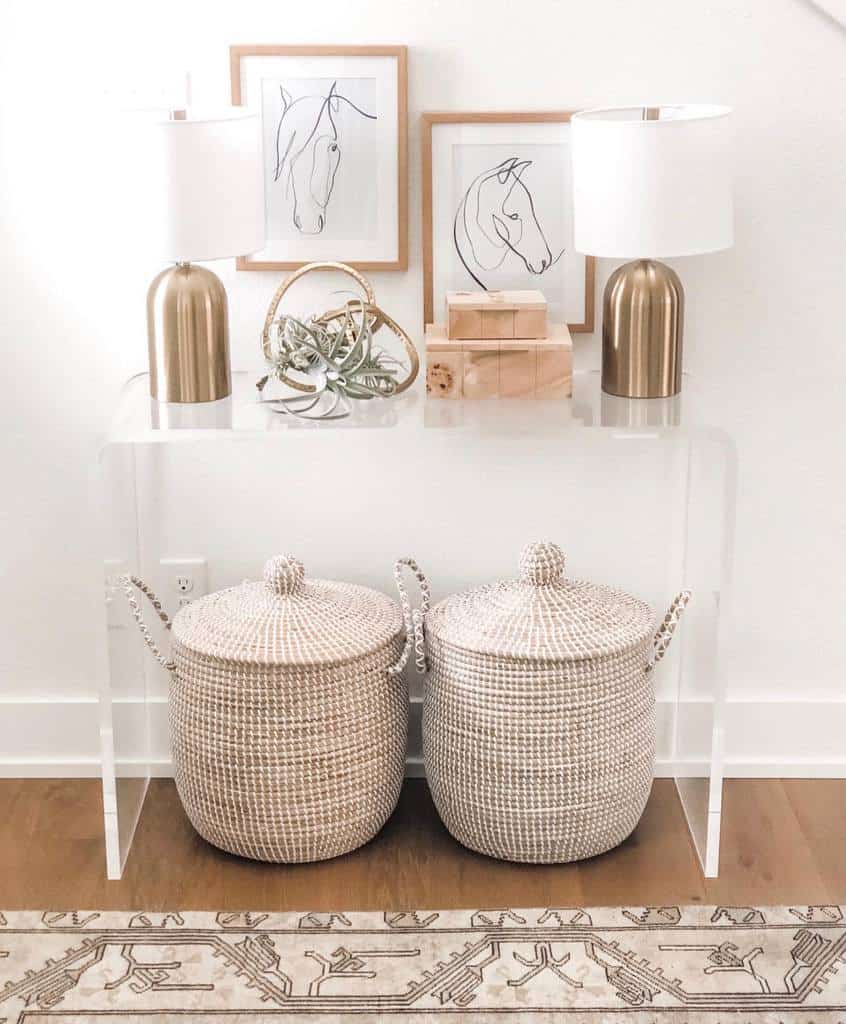 Stylish entryway with a clear acrylic console table, gold lamps, minimalist horse artwork, and woven storage baskets for a chic look