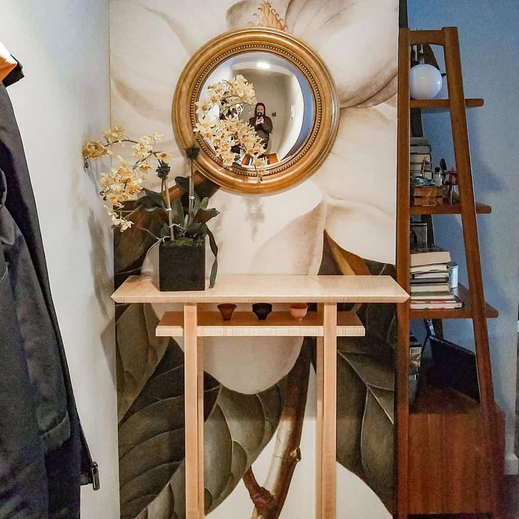 Elegant entryway with a wooden console table, gold-framed mirror, floral mural, and delicate orchid arrangement for a refined touch