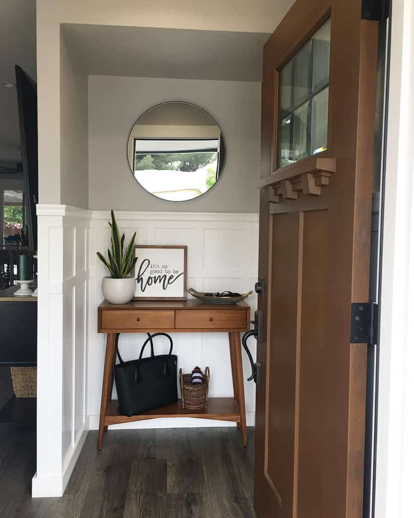 Welcoming entryway with a mid-century console table, round mirror, potted plant, and a cozy 'home' sign for a warm first impression