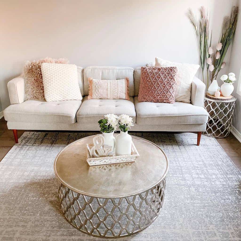 Round metallic coffee table with an intricate lattice base, styled with a tray, vases, and flowers, set in a cozy neutral-toned living room