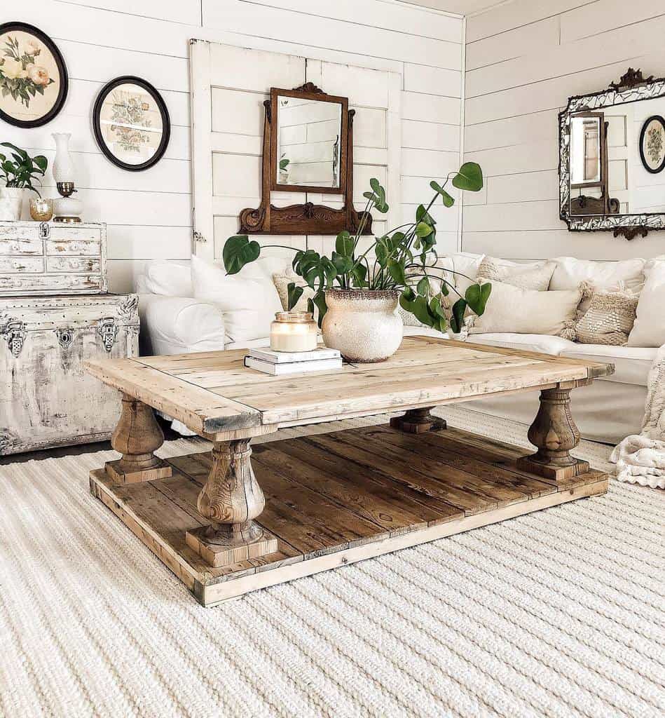 Large rustic wooden coffee table with turned legs and a lower shelf, styled with a potted plant, books, and a candle in a cozy farmhouse living room