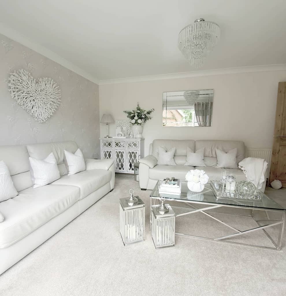 Elegant glass coffee table with a silver metal frame, styled with a tray, candles, and flowers, set in a bright all-white living room