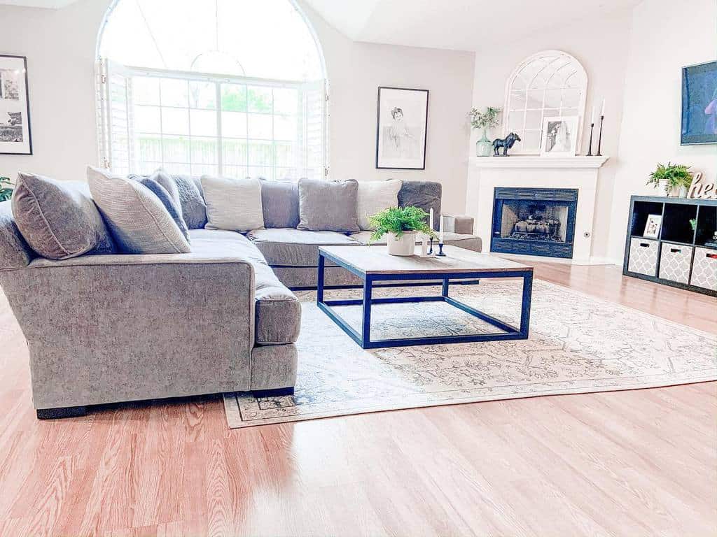 Modern square coffee table with a black metal frame and wooden top, styled with plants and candles, set in a bright living room with a large sectional sofa