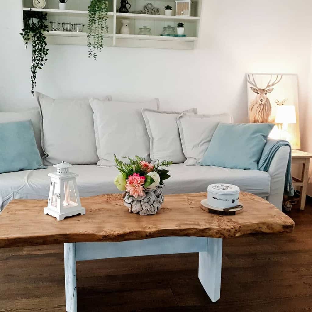 Rustic live-edge wooden coffee table with white legs, styled with a lantern, floral centerpiece, and decorative tin, set in a cozy living room