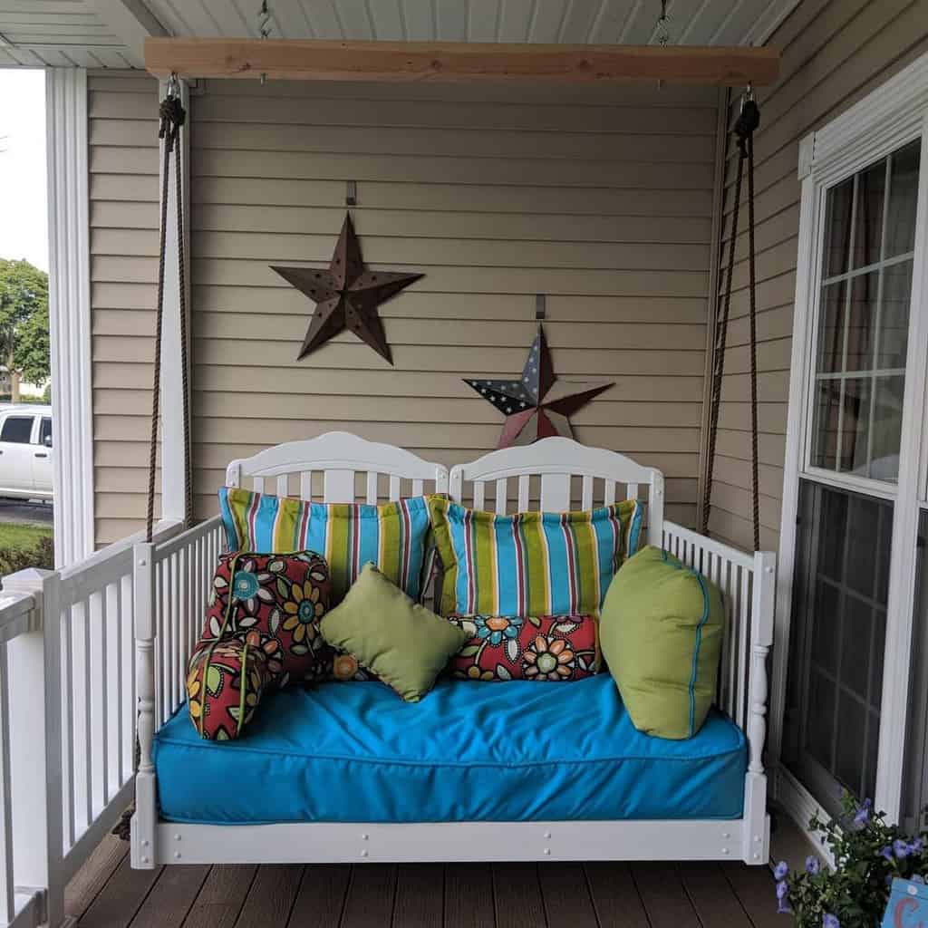 Colorful porch swing with bright cushions and pillows, star-shaped wall decor, and light siding background