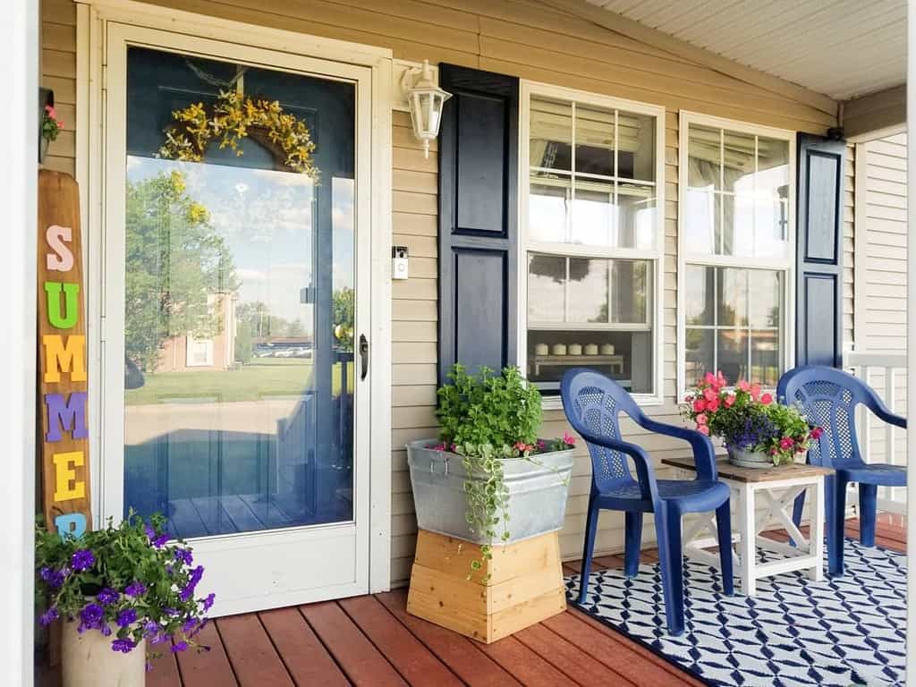 Cheerful porch with blue chairs, a patterned rug, vibrant flowers, and a "Summer" sign, creating a welcoming and colorful entryway