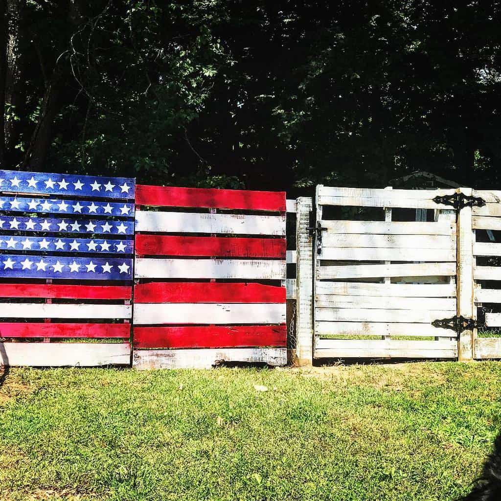 DIY pallet fence painted like the American flag, featuring bold red, white, and blue stripes with stars for a patriotic backyard design