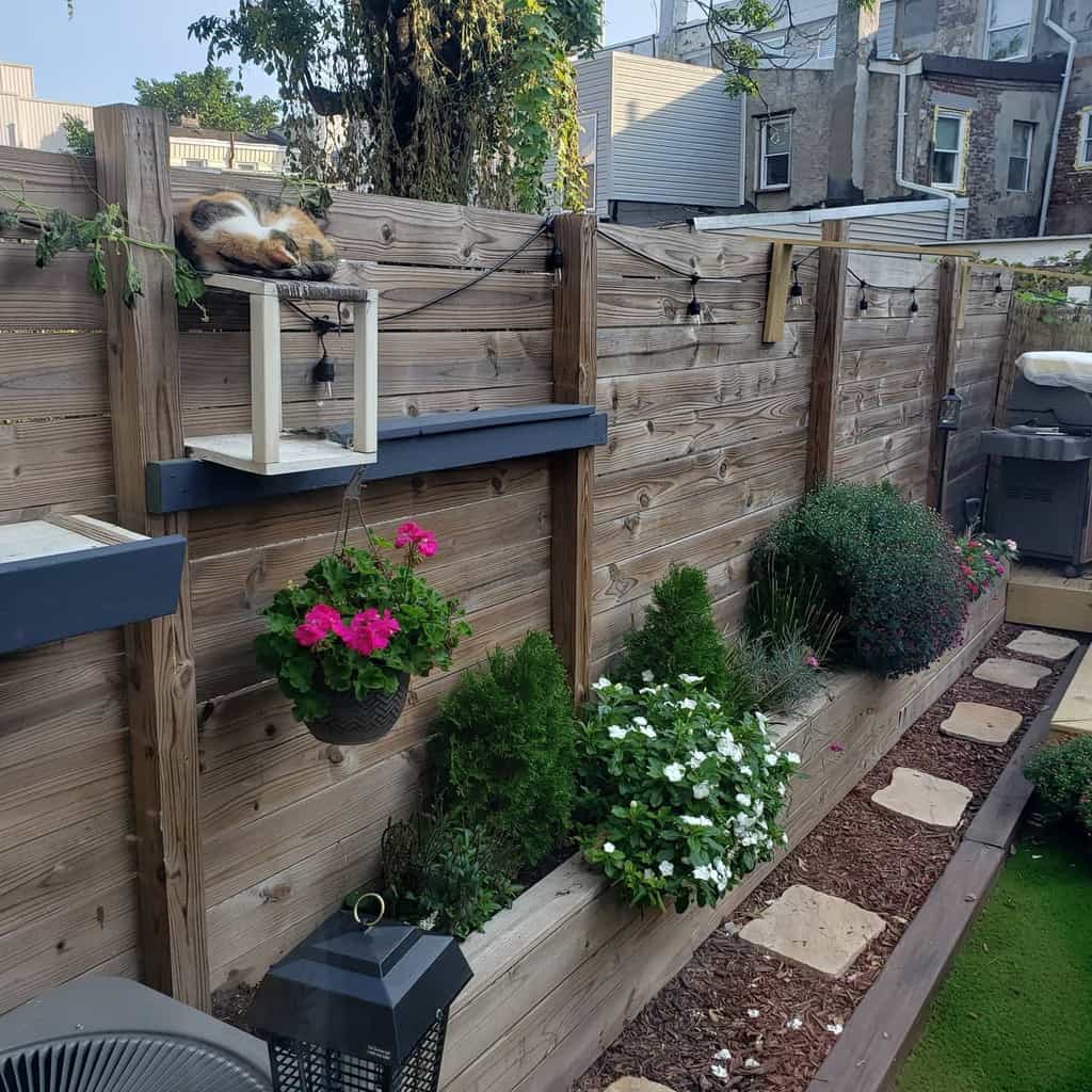 Wooden pallet fence with built-in cat shelves, hanging planters, and lush greenery, creating a cozy and pet-friendly backyard retreat