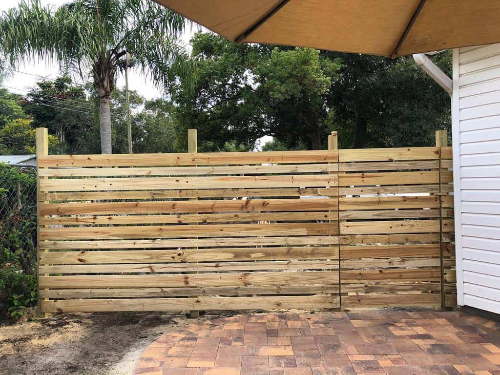 Modern horizontal pallet fence providing partial privacy for a backyard patio, blending natural wood tones with a tropical setting