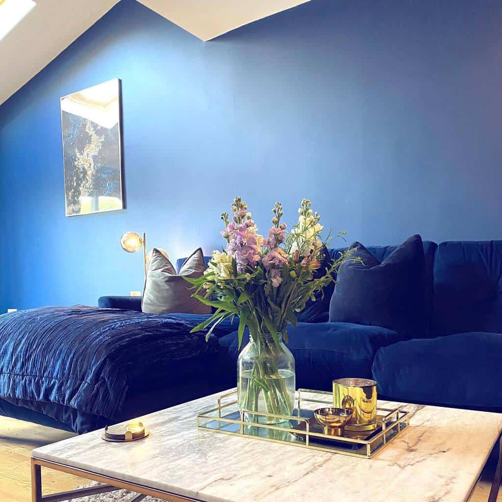 Stylish living room with blue walls and sofa, marble coffee table with flowers and candles, and a modern art piece on the wall