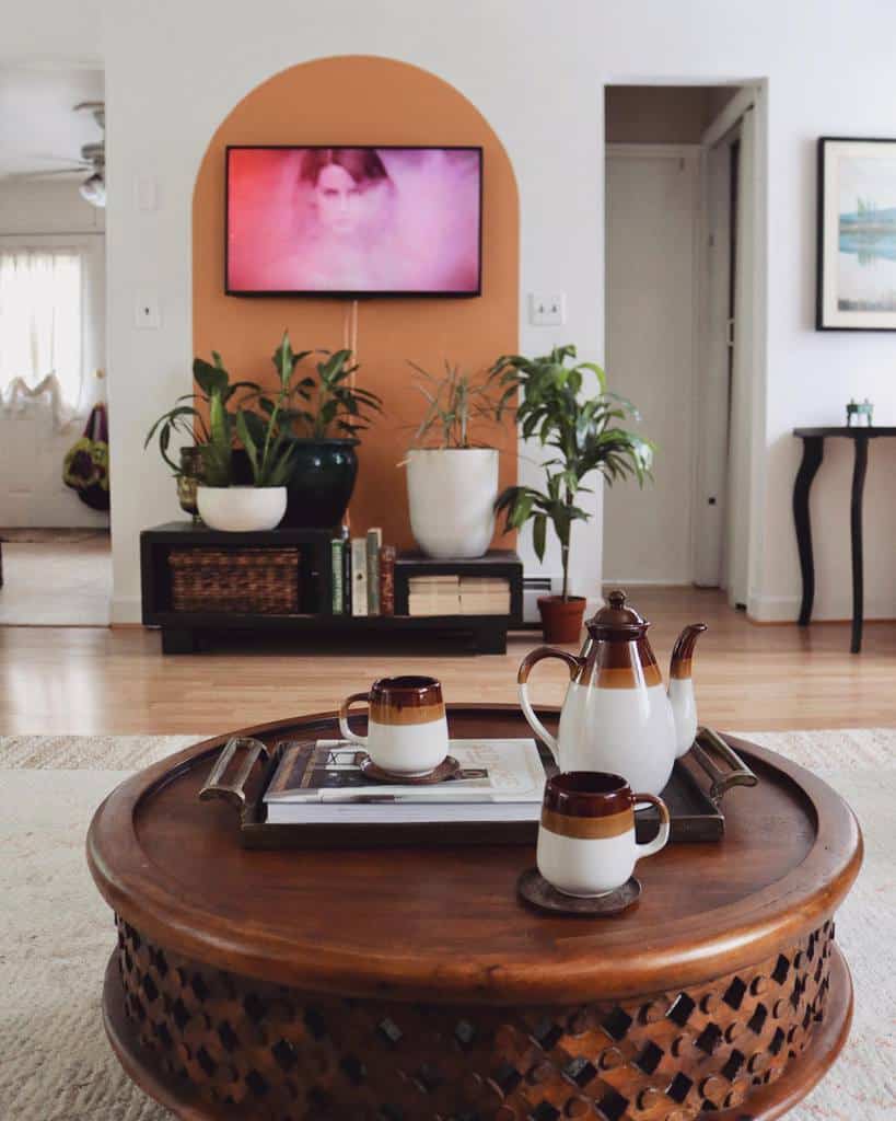 Round wooden coffee table with lattice design, topped with a tray holding a vintage teapot, matching mugs, and books in a cozy living room