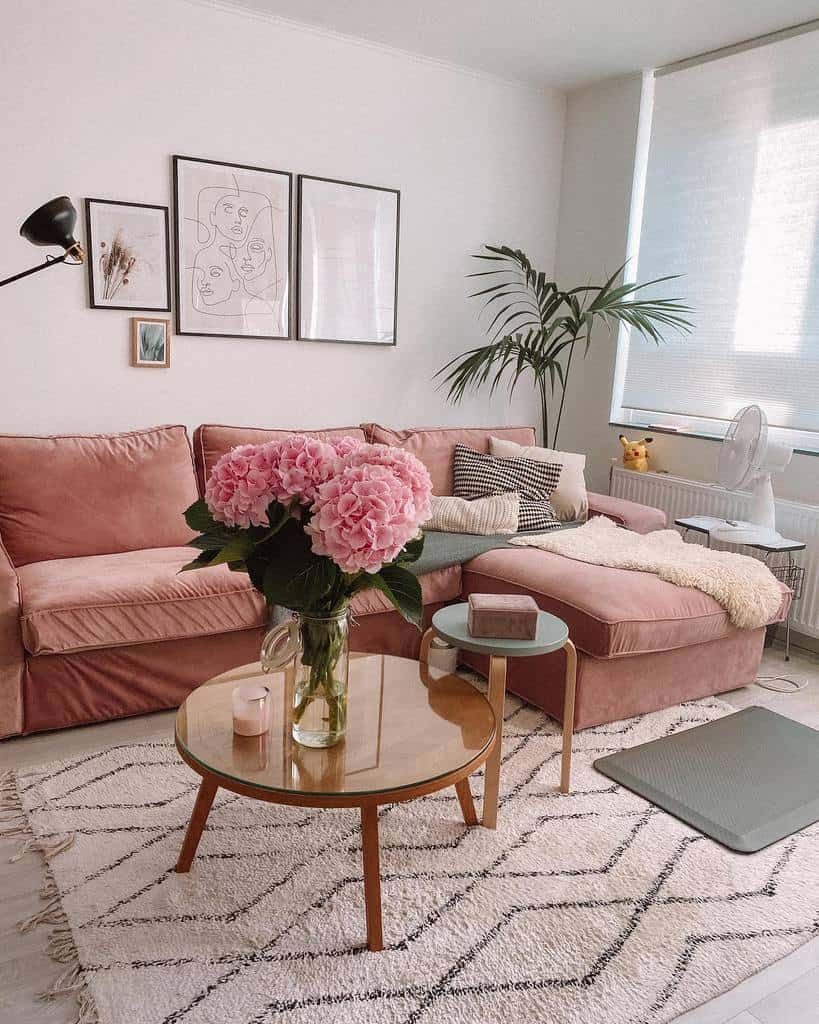 Glass-top wooden coffee table with a vase of pink hydrangeas, set in front of a plush pink sofa in a cozy, modern living room