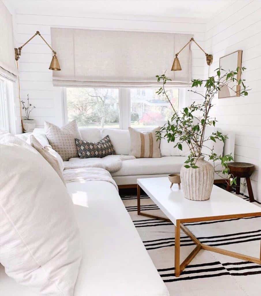 Bright living room with white sofa, patterned cushions, a white coffee table with a vase of branches, and wall-mounted lamps