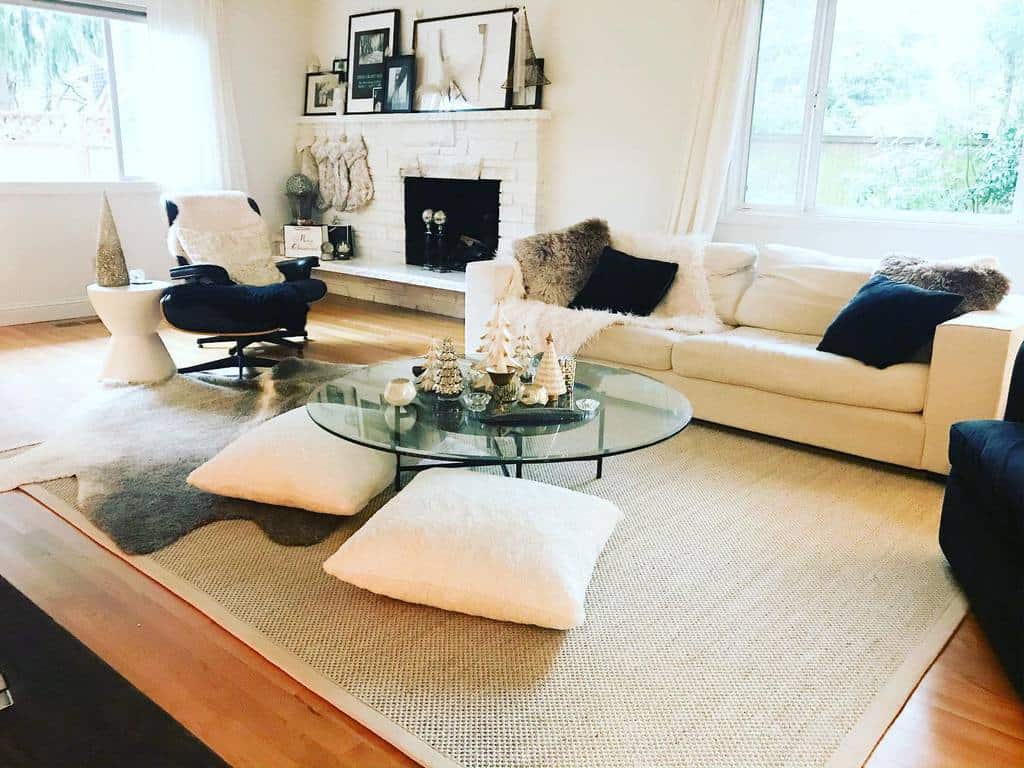 Modern glass coffee table with festive mini trees, surrounded by floor cushions in a cozy living room with a neutral color palette