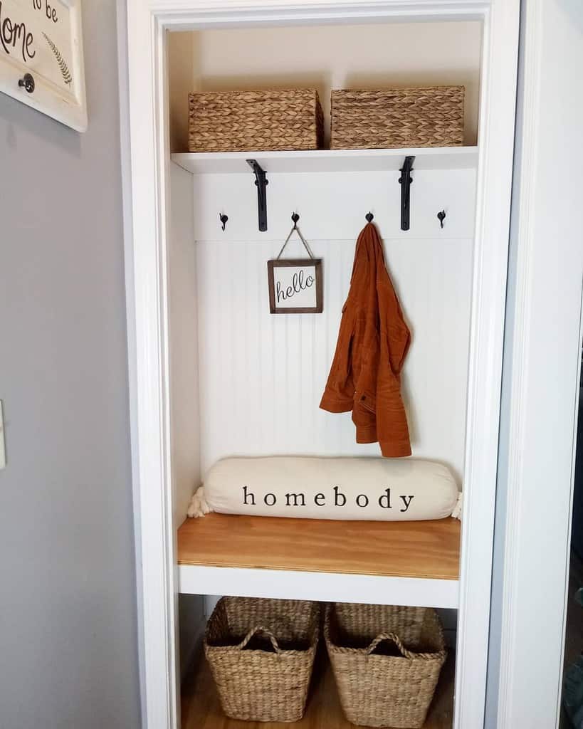 Compact entryway nook with built-in storage, woven baskets, wall hooks, a cozy bench, and a 'homebody' pillow for a welcoming touch