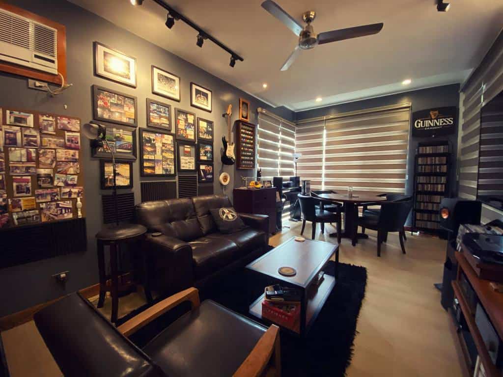 Cozy music-themed room with vinyl records, framed photos, a black leather sofa, a guitar on the wall, and a stylish lounge area