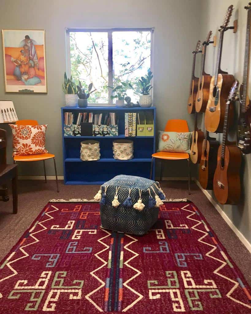 Cozy music room with wall-mounted guitars, a vibrant patterned rug, a blue bookshelf, colorful chairs, and decorative plants