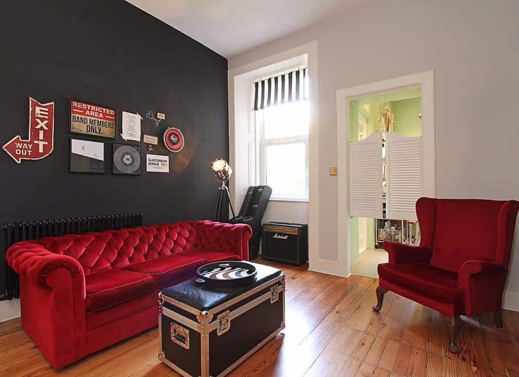 Chic music lounge with red velvet seating, a black accent wall, vintage decor, vinyl records, a Marshall amp, and a stylish trunk table