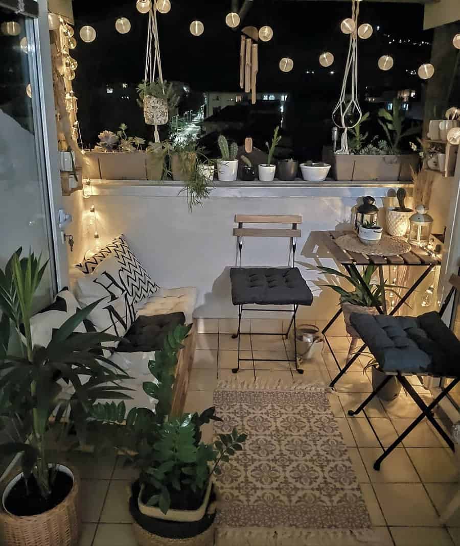 Cozy small balcony at night with string lights, potted plants, a wooden dining set, cushioned seating, and boho-inspired decor