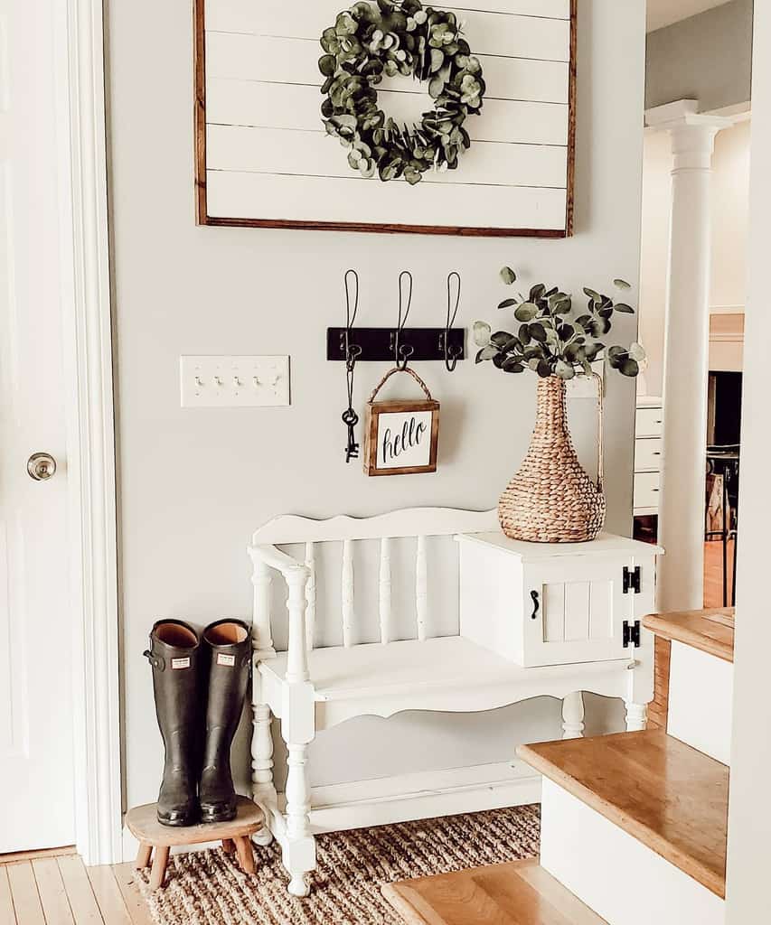 Farmhouse-style entryway with a vintage white bench, woven accents, a greenery wreath, wall hooks, and a cozy rustic decor touch