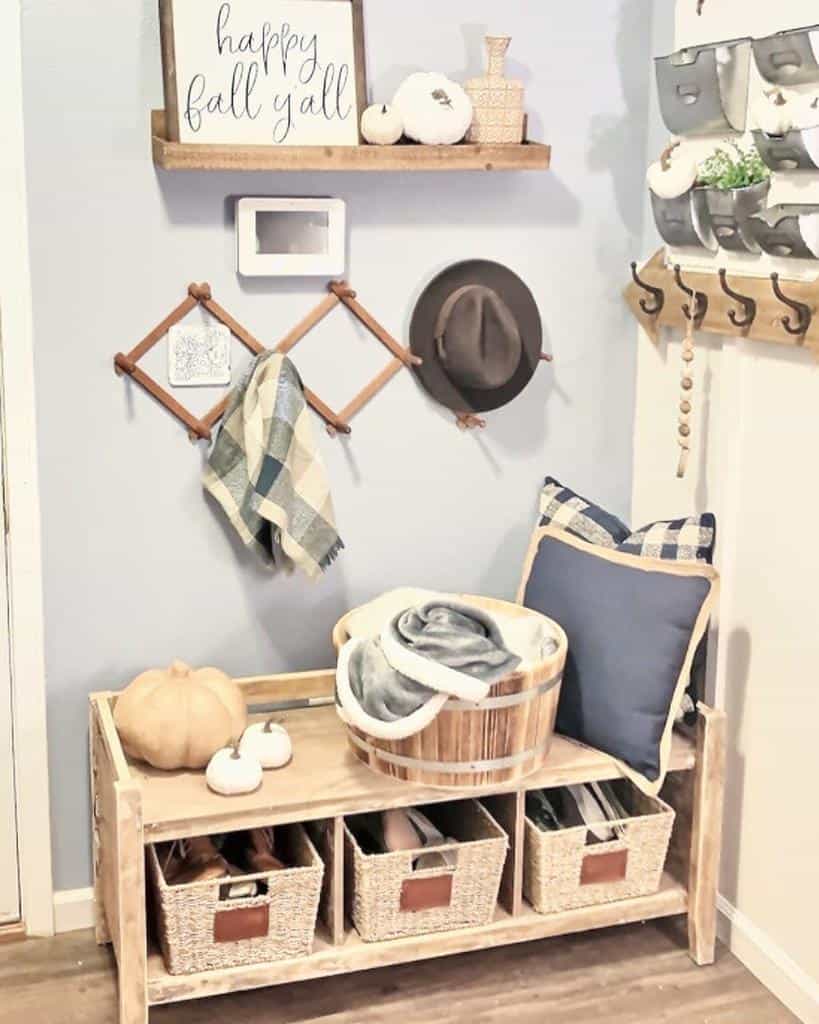 Cozy farmhouse entryway with a wooden storage bench, woven baskets, fall decor, wall hooks, and a welcoming seasonal sign