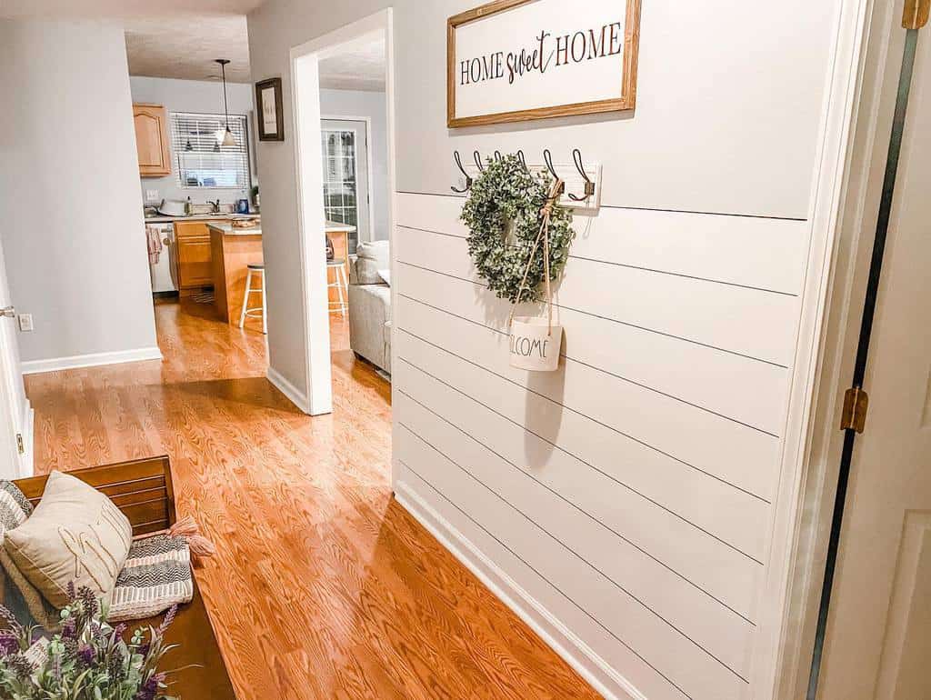 Farmhouse-style entryway with shiplap walls, a 'Home Sweet Home' sign, a greenery wreath, and cozy wooden bench seating