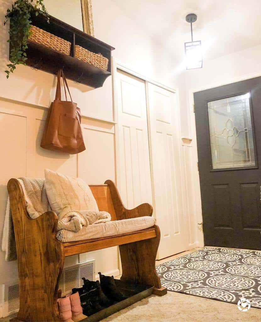 Warm farmhouse entryway with a vintage wooden bench, cozy pillows, a black front door, wall storage, and woven baskets for a rustic touch