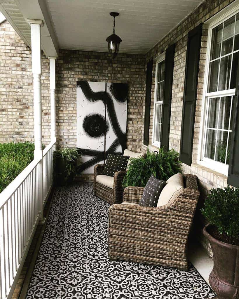 Front porch with wicker chairs, patterned rug, potted plants, abstract black-and-white art, and brick wall