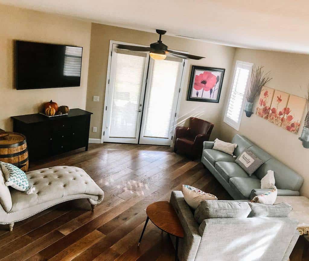 Small living room with a sofa, chaise lounge, armchairs, wall art, TV, ceiling fan, and double doors leading outside.