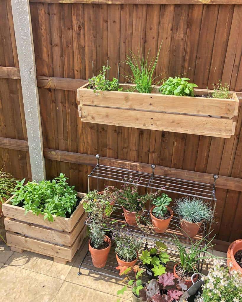 DIY wooden pallet planters mounted on a brown fence, filled with fresh herbs and greenery, creating a charming vertical garden