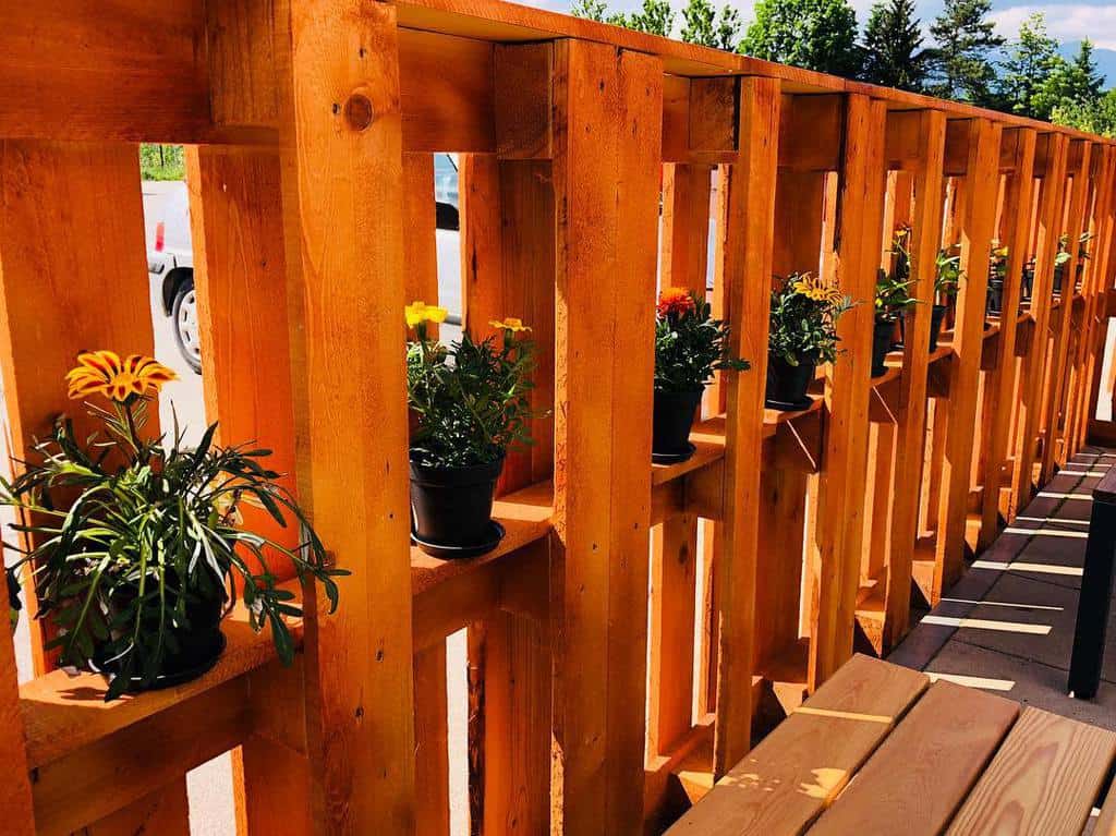 Wooden pallet fence with built-in shelves holding potted flowers, creating a warm and inviting outdoor space with a natural touch