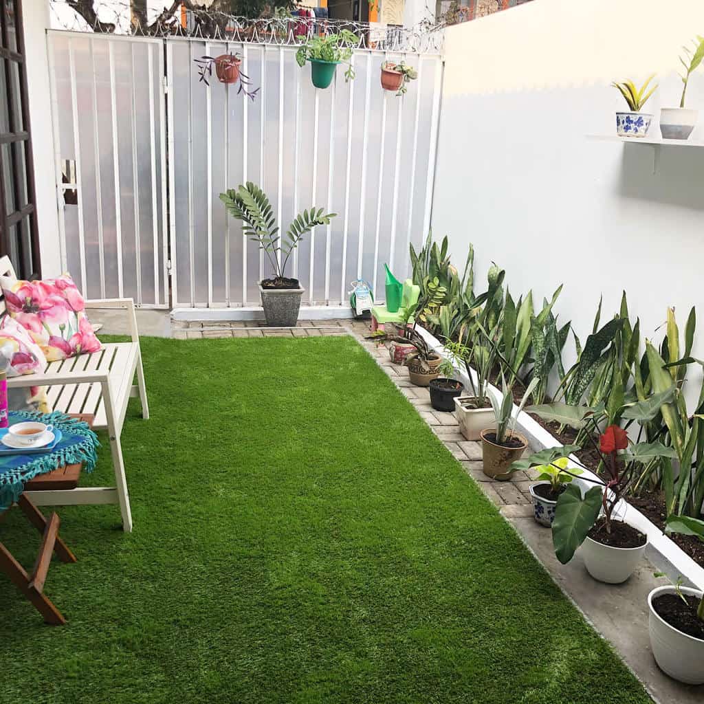 Cozy patio with green artificial grass, potted plants, a white bench, and a small table with a cup and saucer on a colorful cloth