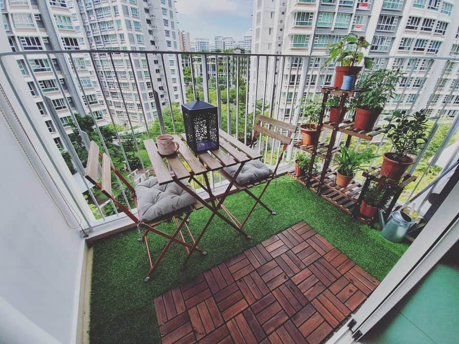 Modern high-rise balcony with artificial grass, wooden flooring, a cozy bistro set, potted plants, and a scenic city view