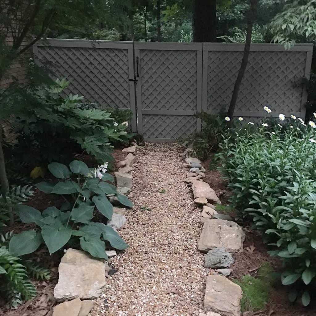 Gravel path lined with stones and lush plants leads to a lattice gate in a garden setting