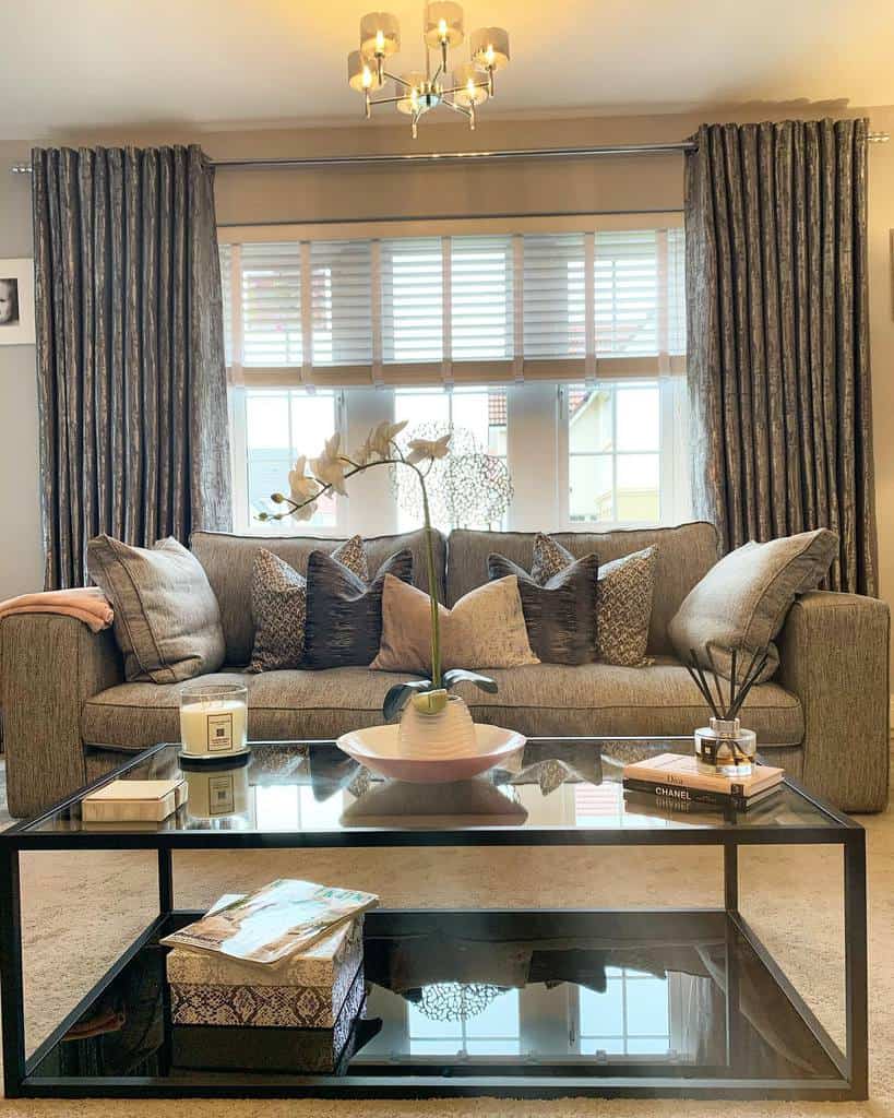 Modern glass coffee table with a black metal frame, styled with a vase, books, and candles, set in an elegant living room with plush decor