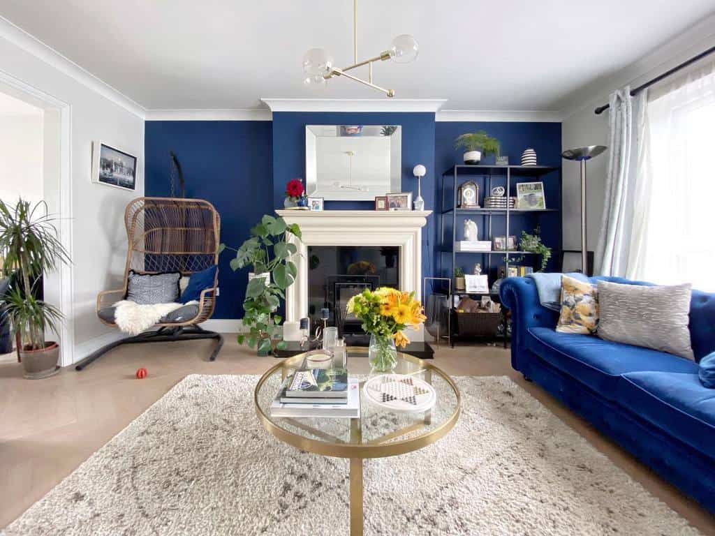 Round glass coffee table with a gold metal frame, styled with books, a vase of yellow flowers, and candles, set in a bold blue and white living room