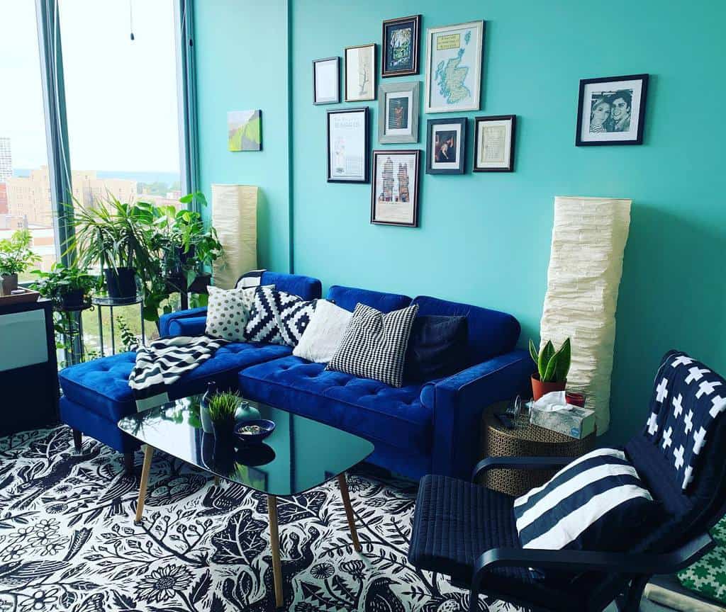 Modern black glass coffee table with wooden legs, styled with a small plant and bowl, set in a vibrant living room with teal walls and a blue sofa