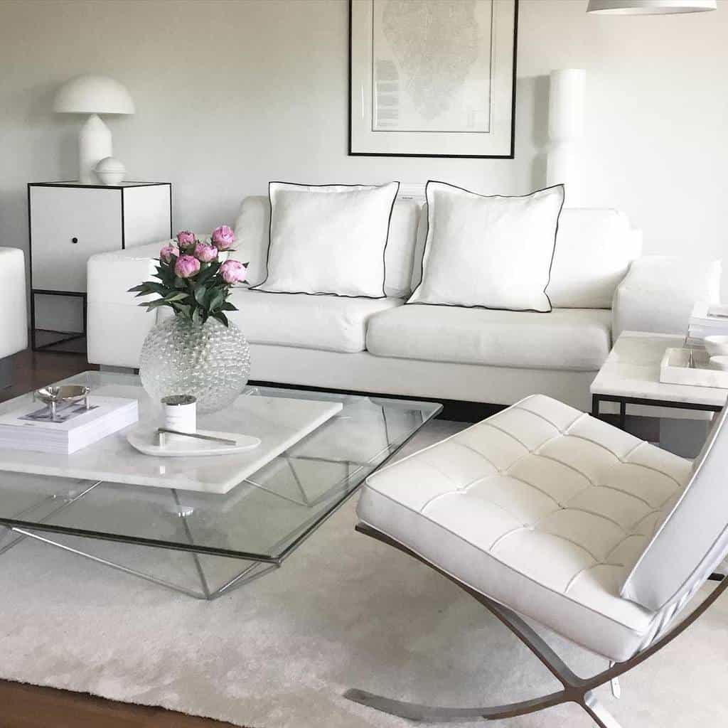 Minimalist white living room with a square glass coffee table, white sofa, modern chair, and pink flowers in a vase