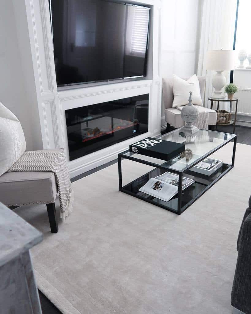 Modern glass coffee table with a black metal frame and lower shelf, styled with books and decor, set in a sleek neutral-toned living room