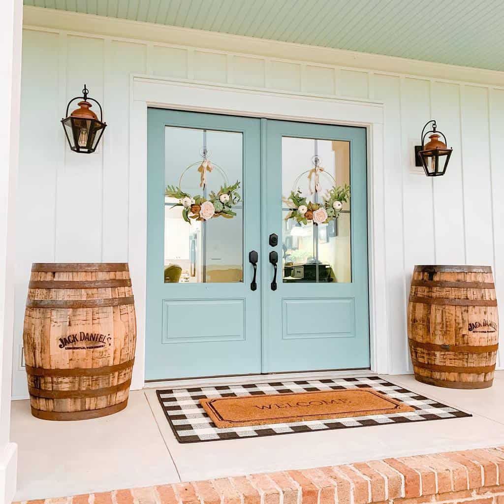 A charming porch with double turquoise doors, floral wreaths, lanterns, Jack Daniel's barrels, and a welcome mat