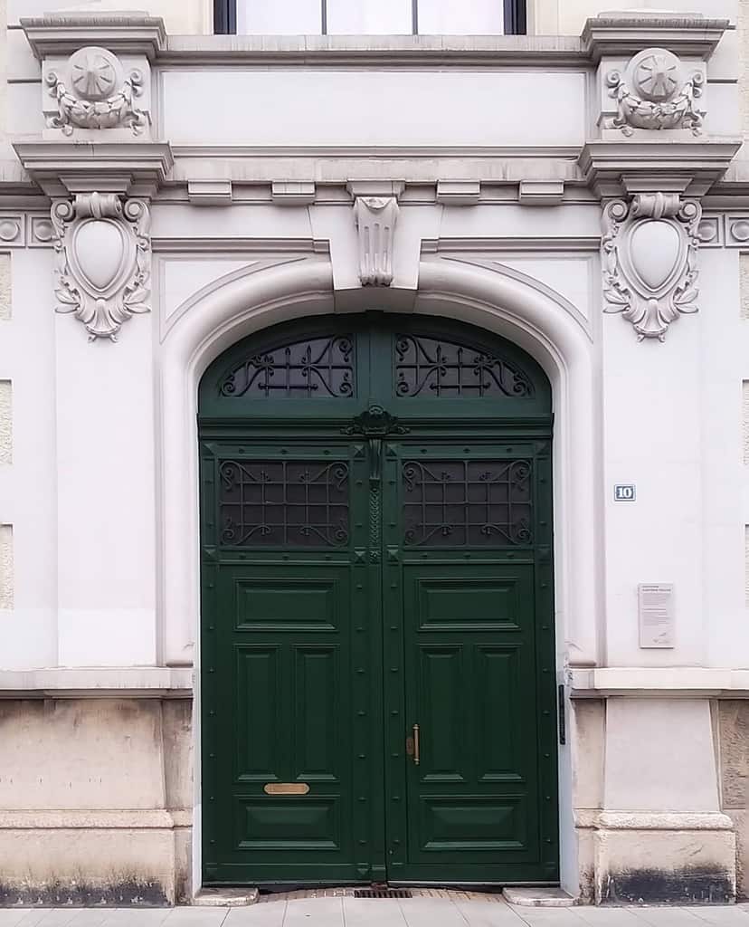 Elegant green double doors with ornate white stone arch and decorative details on a historic building façade