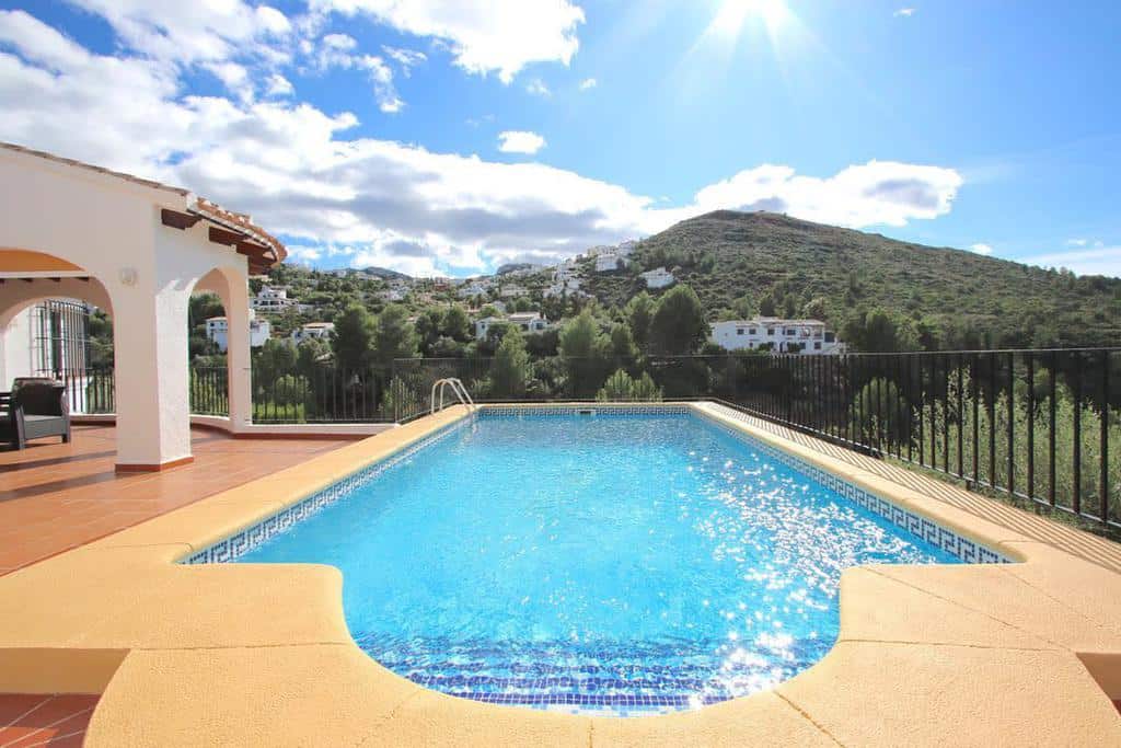 Outdoor pool with clear blue water, surrounded by a tiled deck and a mountainous backdrop under a sunny sky