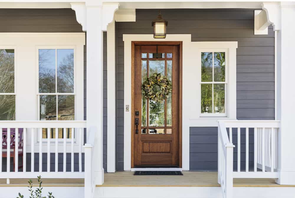 Front porch with blue siding, a wooden door with glass panels, a wreath, white trim, windows on each side, and a hanging lantern above