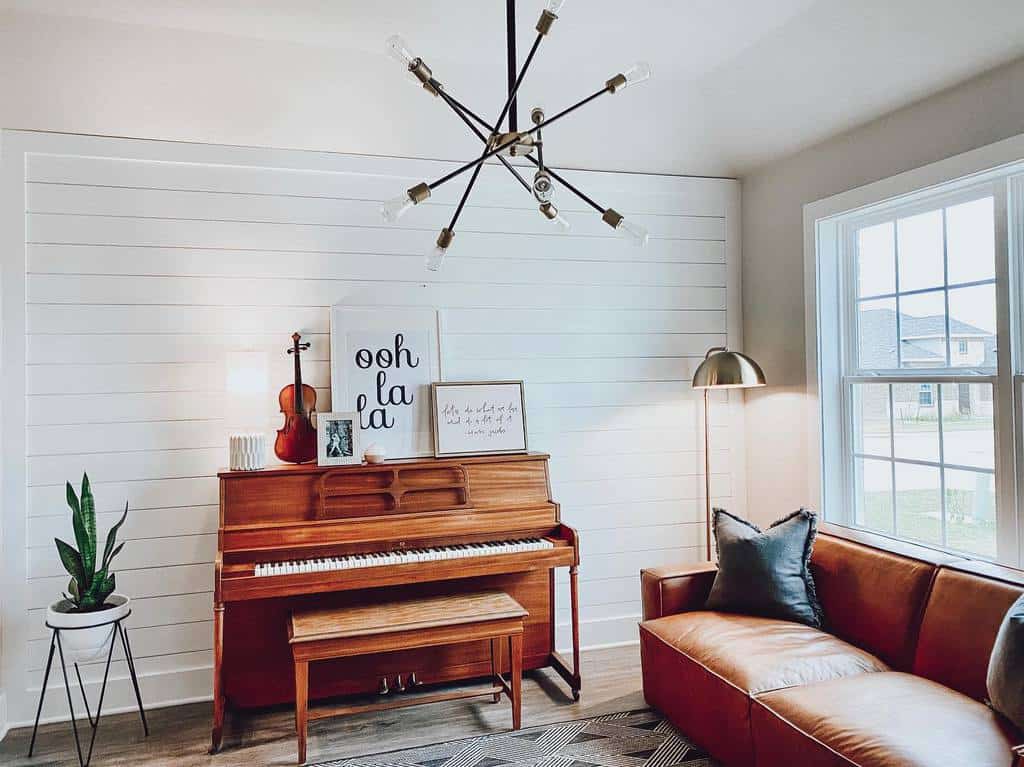 Cozy music room with a vintage upright piano, violin, modern chandelier, leather sofa, and minimalist decor with warm wood tones