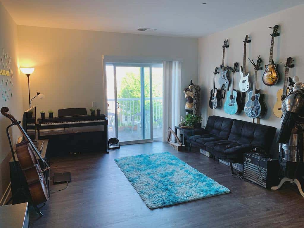 Spacious music room with wall-mounted guitars, a keyboard, a cello, a black sofa, a blue rug, and a balcony view