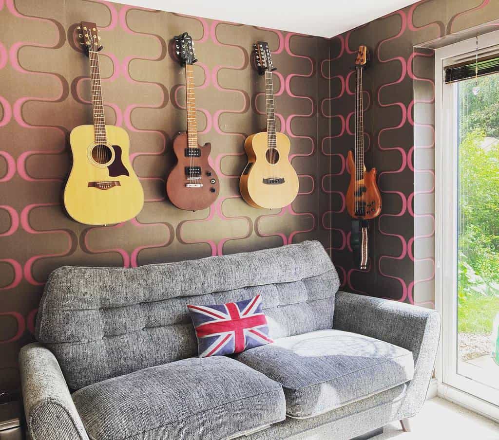 Cozy music nook with wall-mounted guitars, a retro-patterned wall, a gray sofa, a Union Jack pillow, and natural light from a window