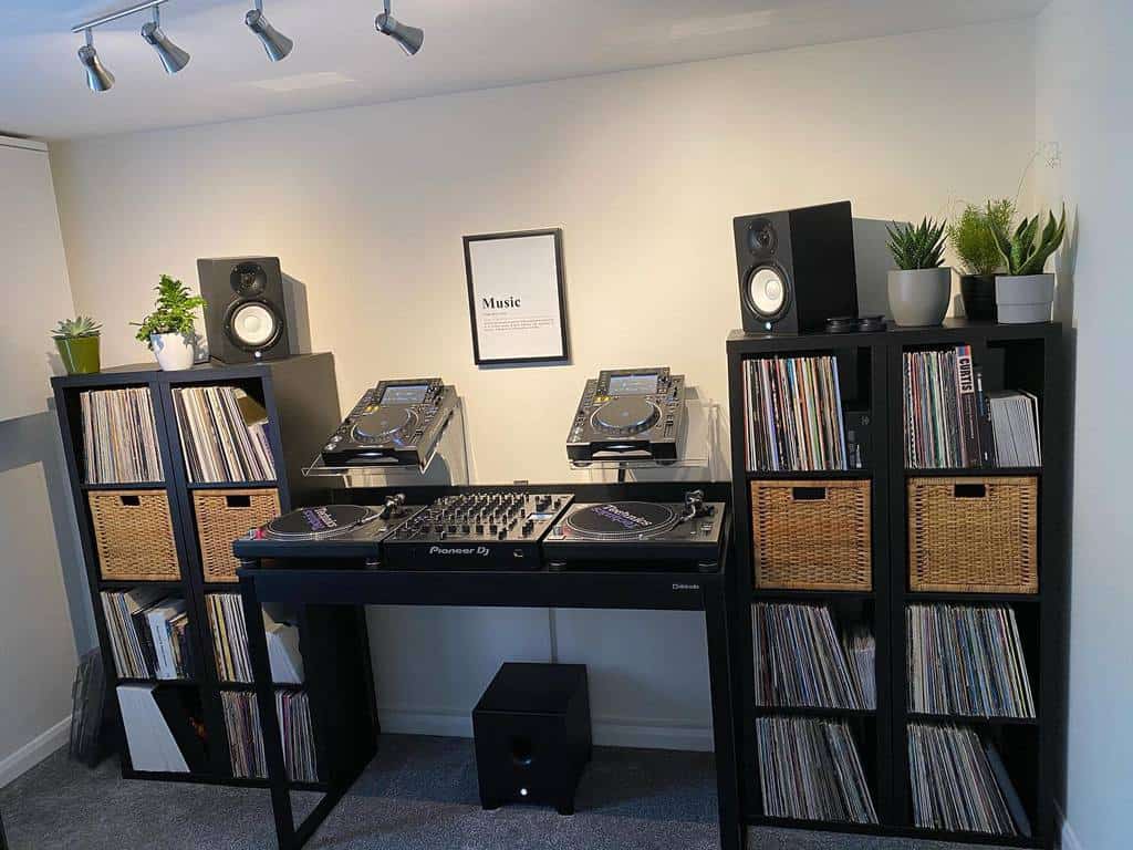 Modern DJ setup with Pioneer turntables, vinyl record storage, studio speakers, ambient lighting, and decorative plants in a sleek music room